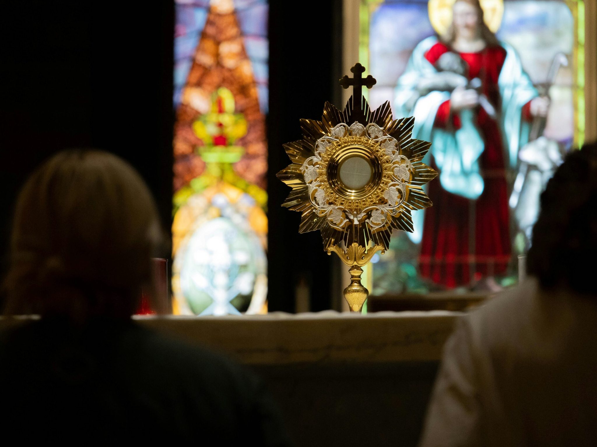 Golden monstrance displayed before stained-glass windows during Eucharistic adoration